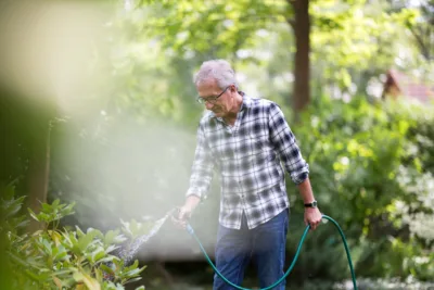 Vieux monsieur jardinier à domicile bientôt à la retraite et arrosant le jardin de son particulier employeur.